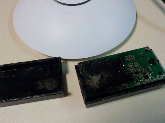 A white UniFi wifi access point dish.
In front is the power injector that is open, with the back of the PCB having half of its surface black from a burn.