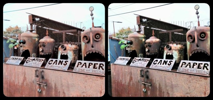 Four rusty propane tanks turned into faux robot heads over a recycling bin. They are labeled Landfill, Compost, Cans, and Paper.