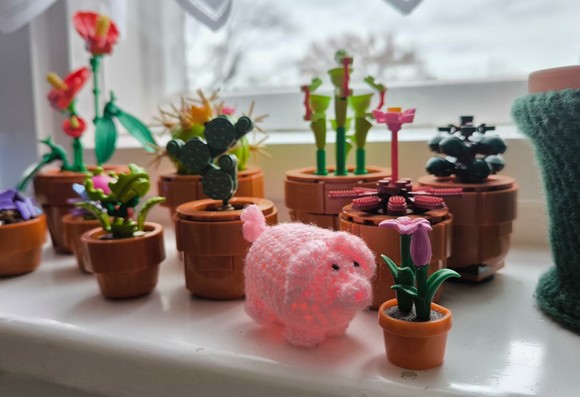 Ein haekelschwein auf einer Fensterbank inmitten von Lego-Topfpflanzen.
