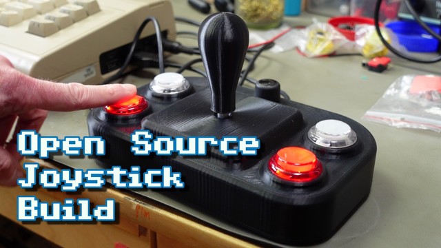 Thumbnail for my video. A fancy 3d printed joystick on my workbench with my index finger pushing one of the fire buttons. The overlayed text reads "Open Source Joystick Build".