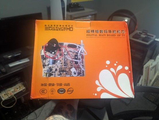 My hand holding up an orange box of Digital Main Board of TV (for CRT TVs).