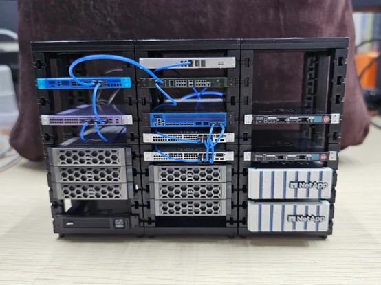 A little tiny datacenter in someone’s house with 3 racks and various brand names and tiny fake ethernet cables