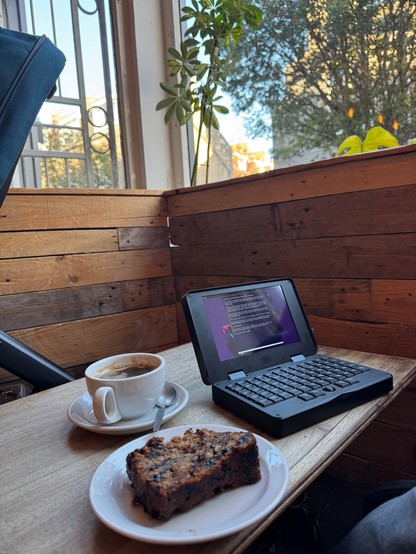 A cup of coffee, some banana bread and a pocket reform laptop on a wooden table