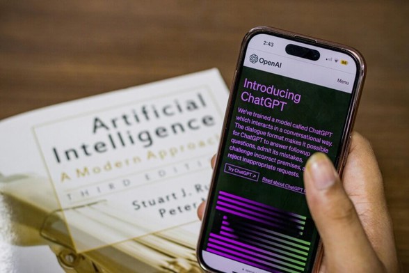 Jemand schaut sich auf dem Smartphone eine Einführung in ChatGPT an. Im Hintergrund liegt ein Buch über KI.