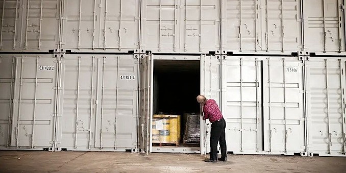 Photo of Brewster Kahle at the Internet Archive’s physical archive site. He is leaning forward and looking into a large shipping container used for storage, with palettes visible inside.