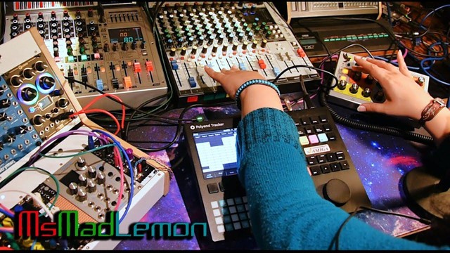 Maddi with one hand on her mixing console and another on the moog sirin synthesizer with a modular synth next to her.
