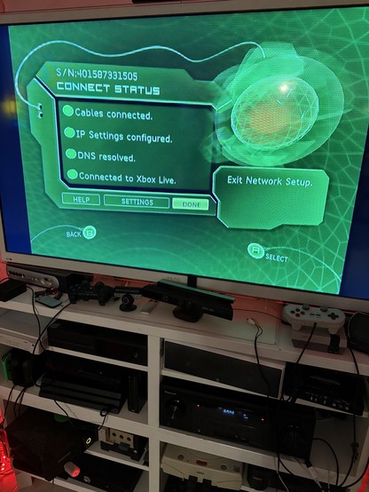 Original XBOX in a shelf full of other consoles, turned on, showing successful connect to XBOX Live (Insignia Service)